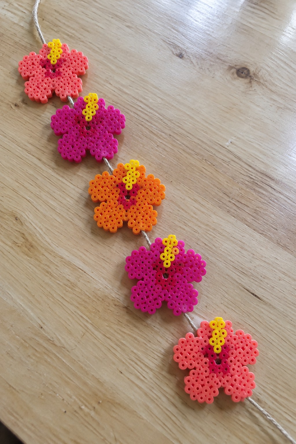 Colorful perler bead flowers in pink and orange strung on twine over wood