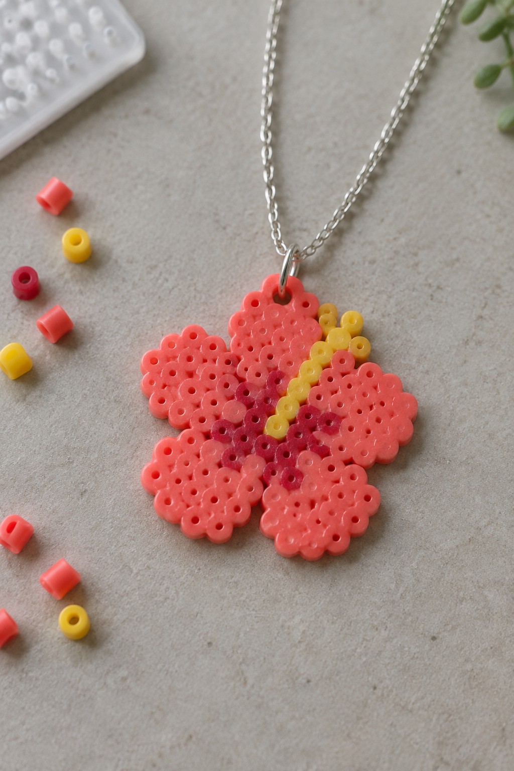 Pink perler bead flower pendant necklace with loose beads on gray surface