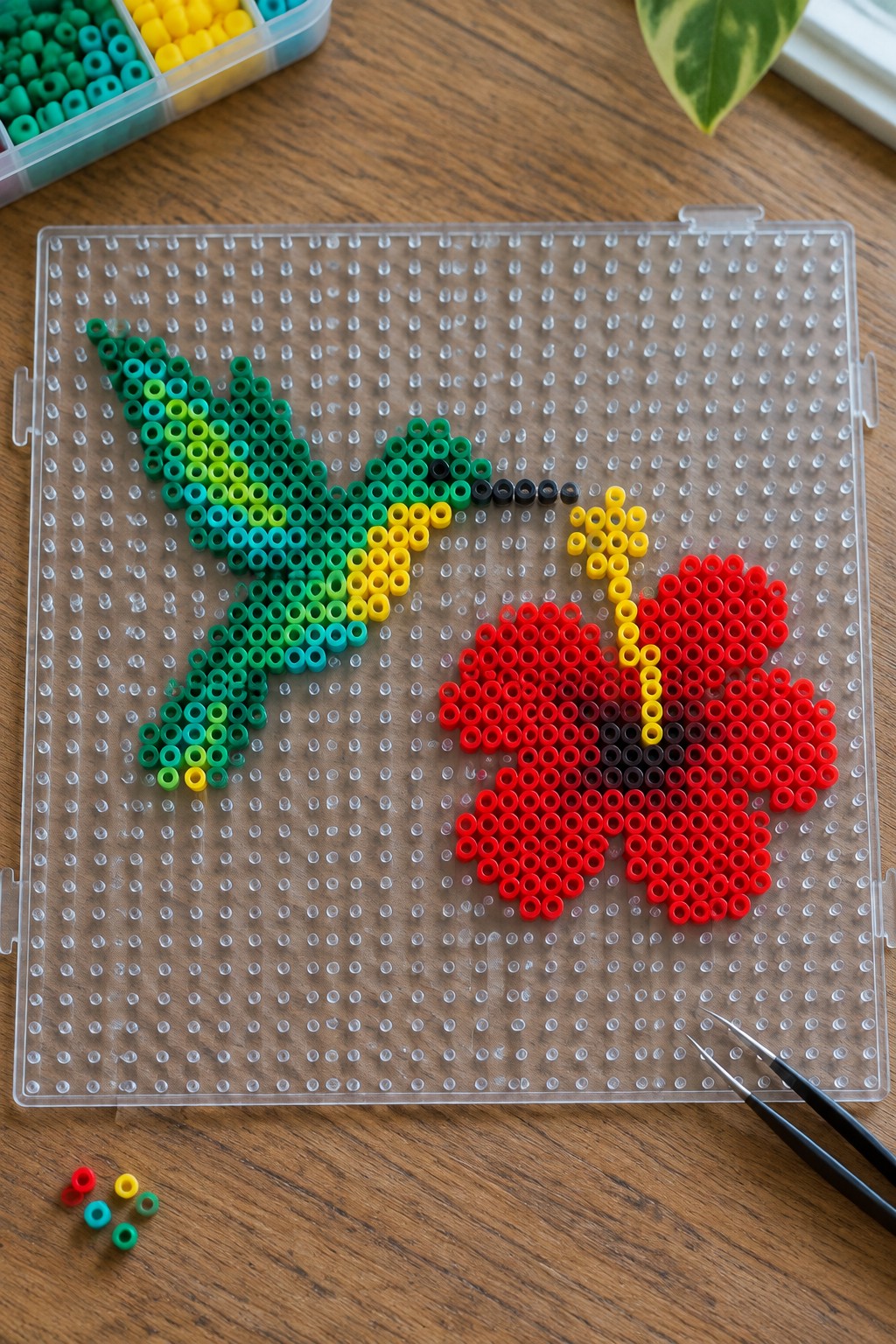Green hummingbird and red flower perler bead art on clear pegboard with supplies