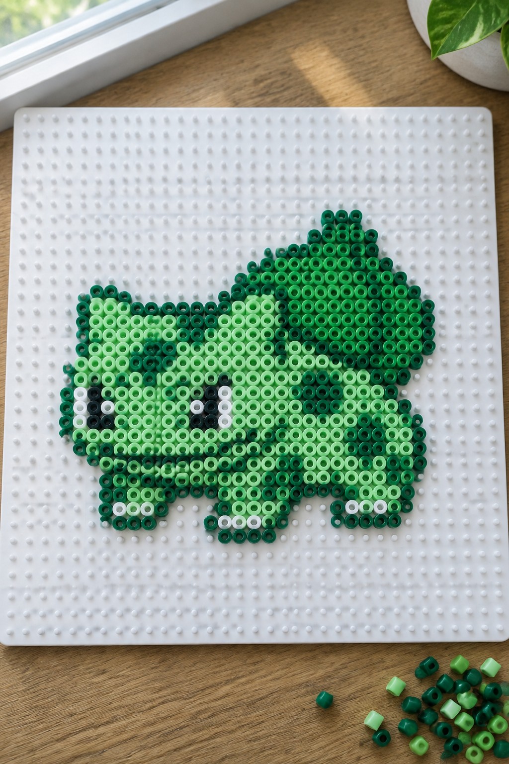 Green Perler beads forming a frog on white pegboard with loose beads nearby