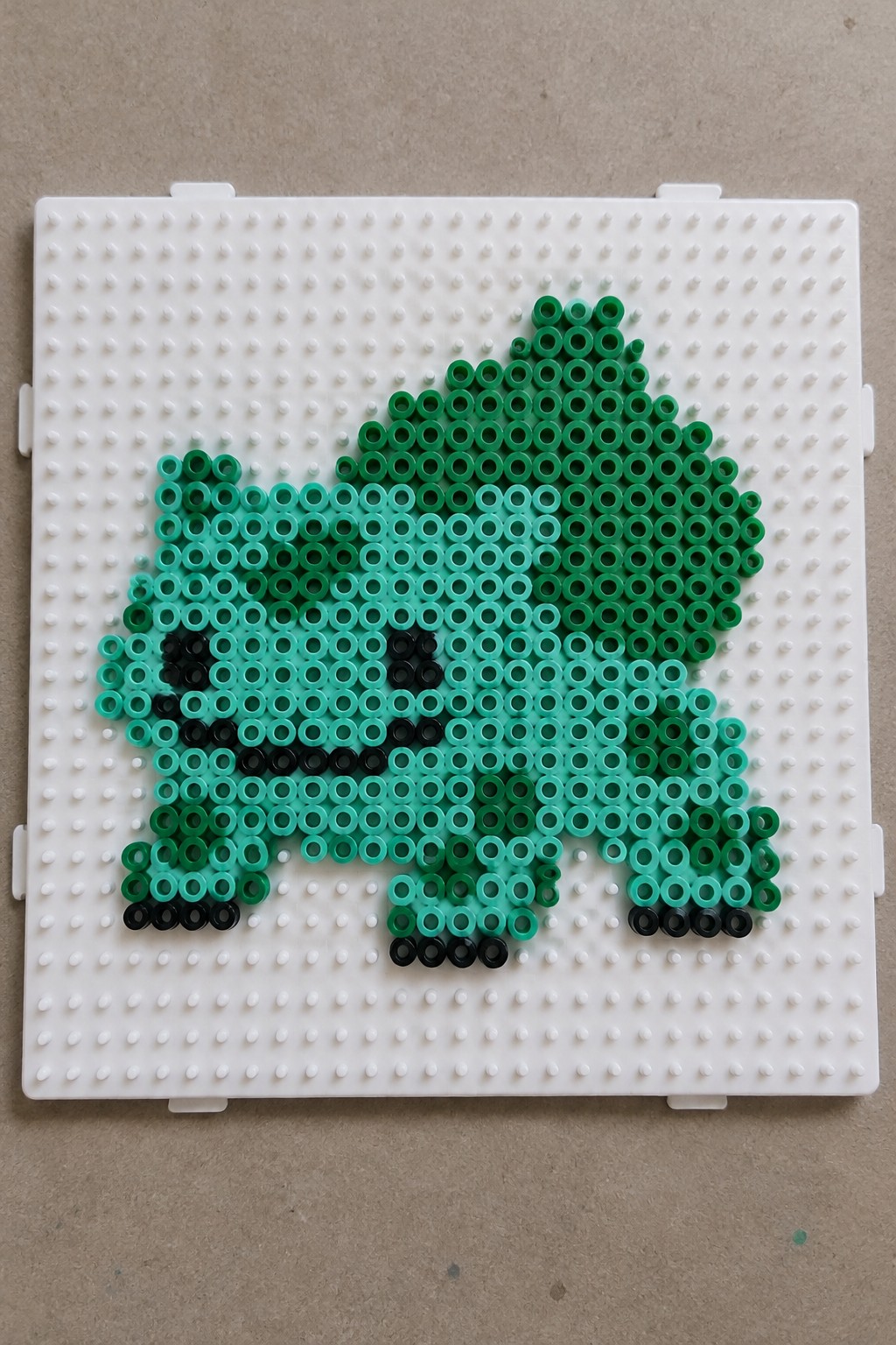 Green perler bead Bulbasaur on white pegboard with black eyes and feet