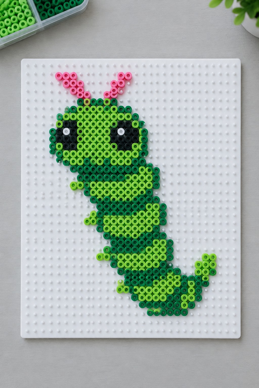 Green perler bead caterpillar with pink antennae on white pegboard