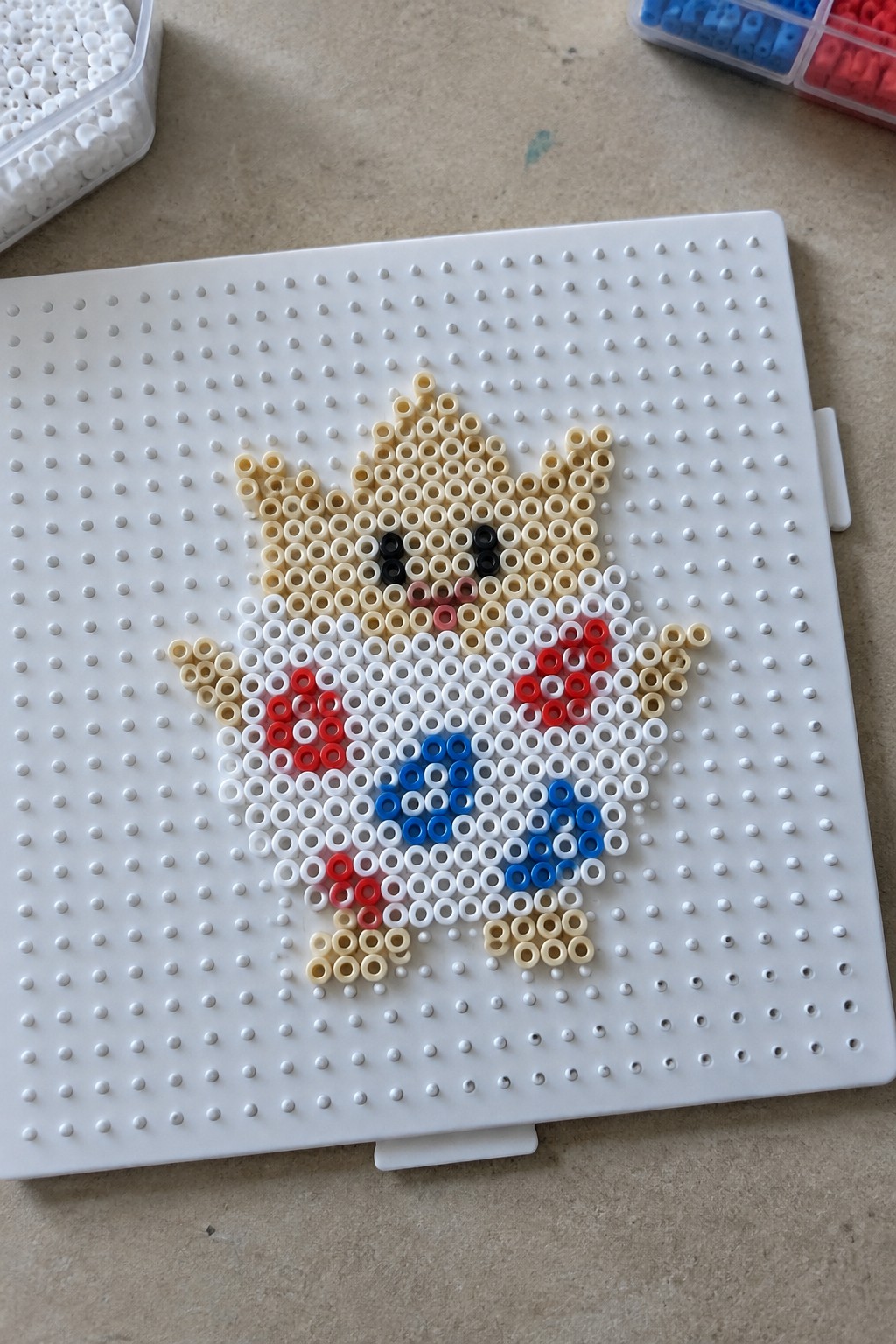 Crowned perler bead figure with red, white, blue accents on white pegboard