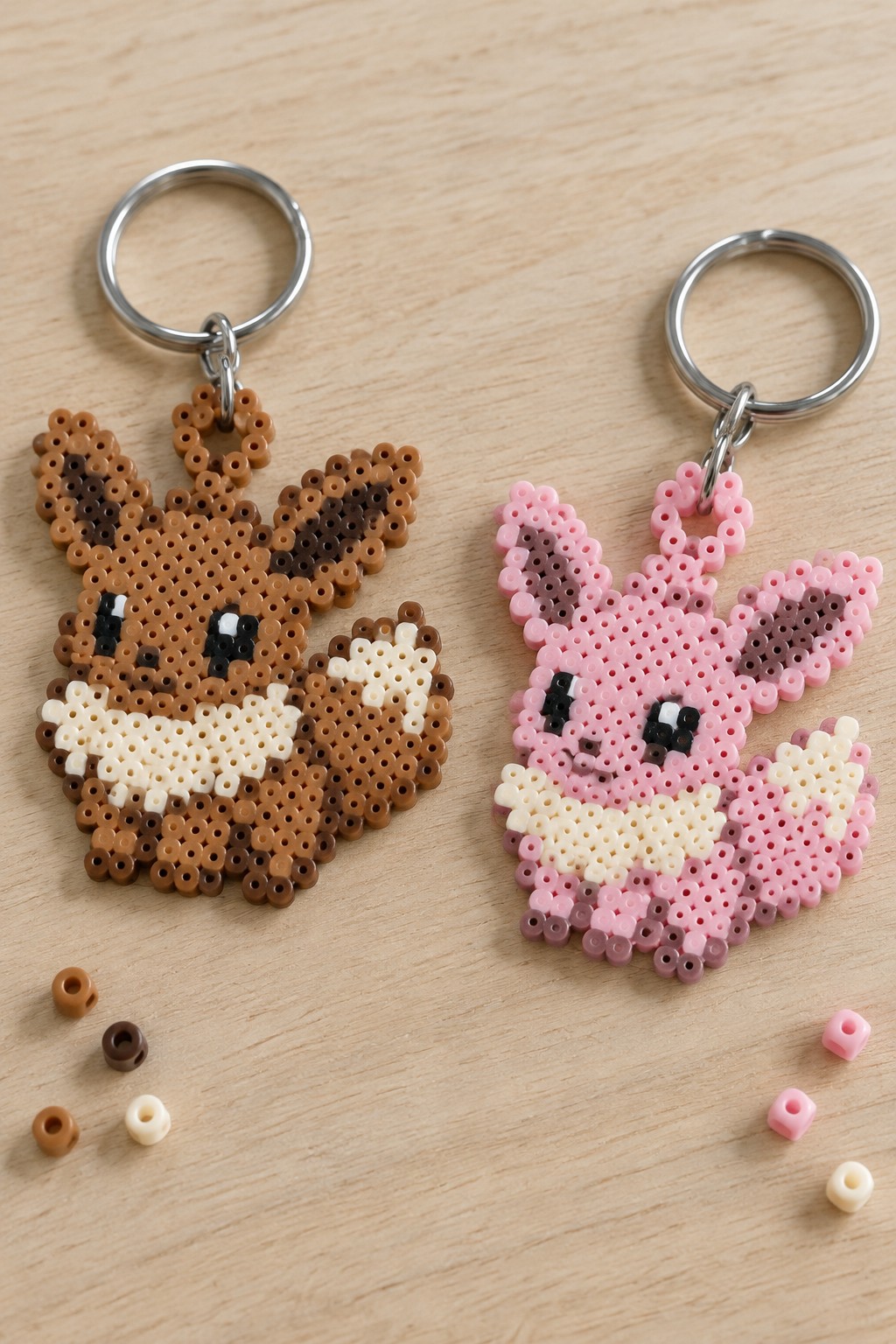 Brown and pink perler bead Eevee keychains on wood with loose beads