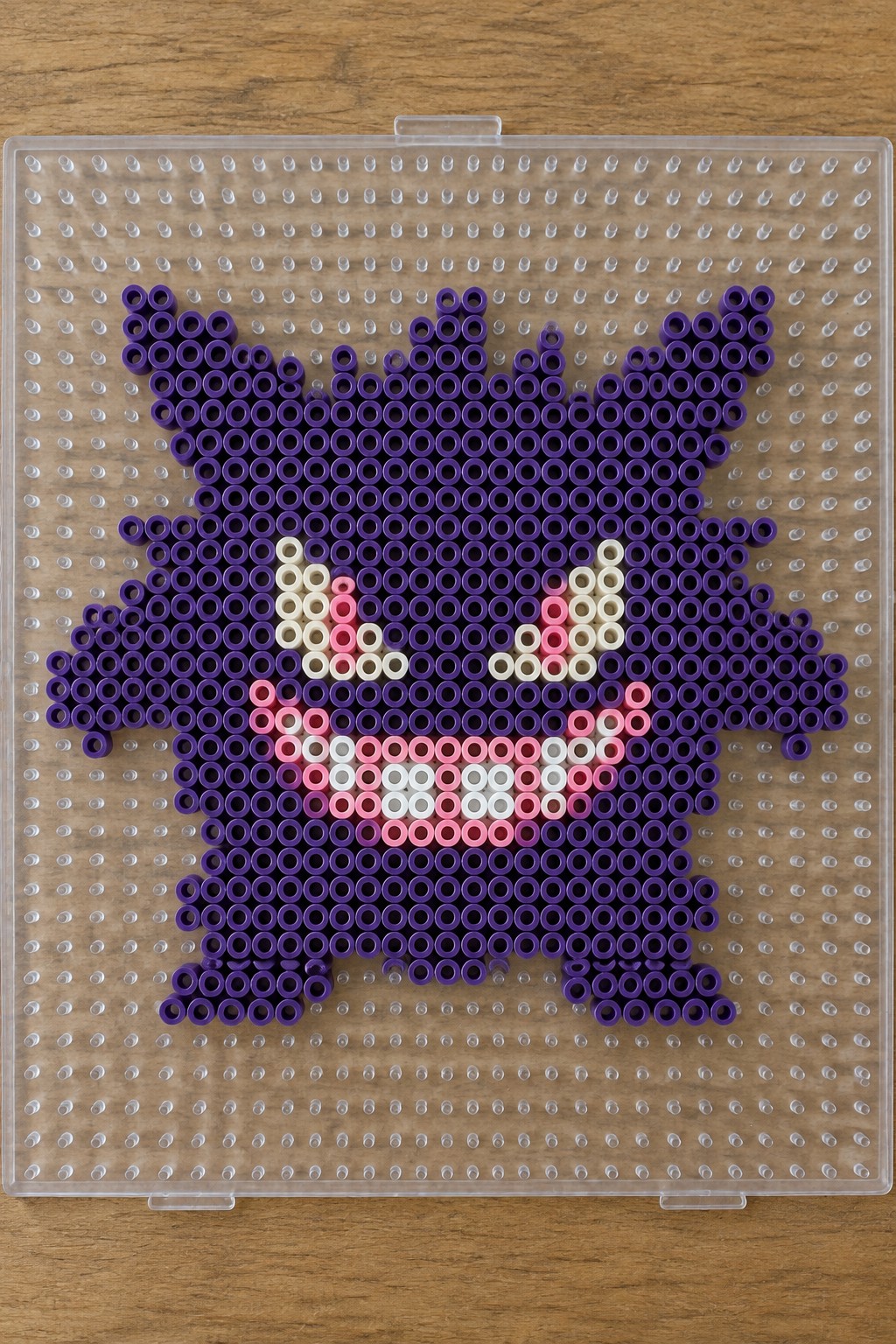 Purple Perler bead Gengar on clear pegboard over wood surface