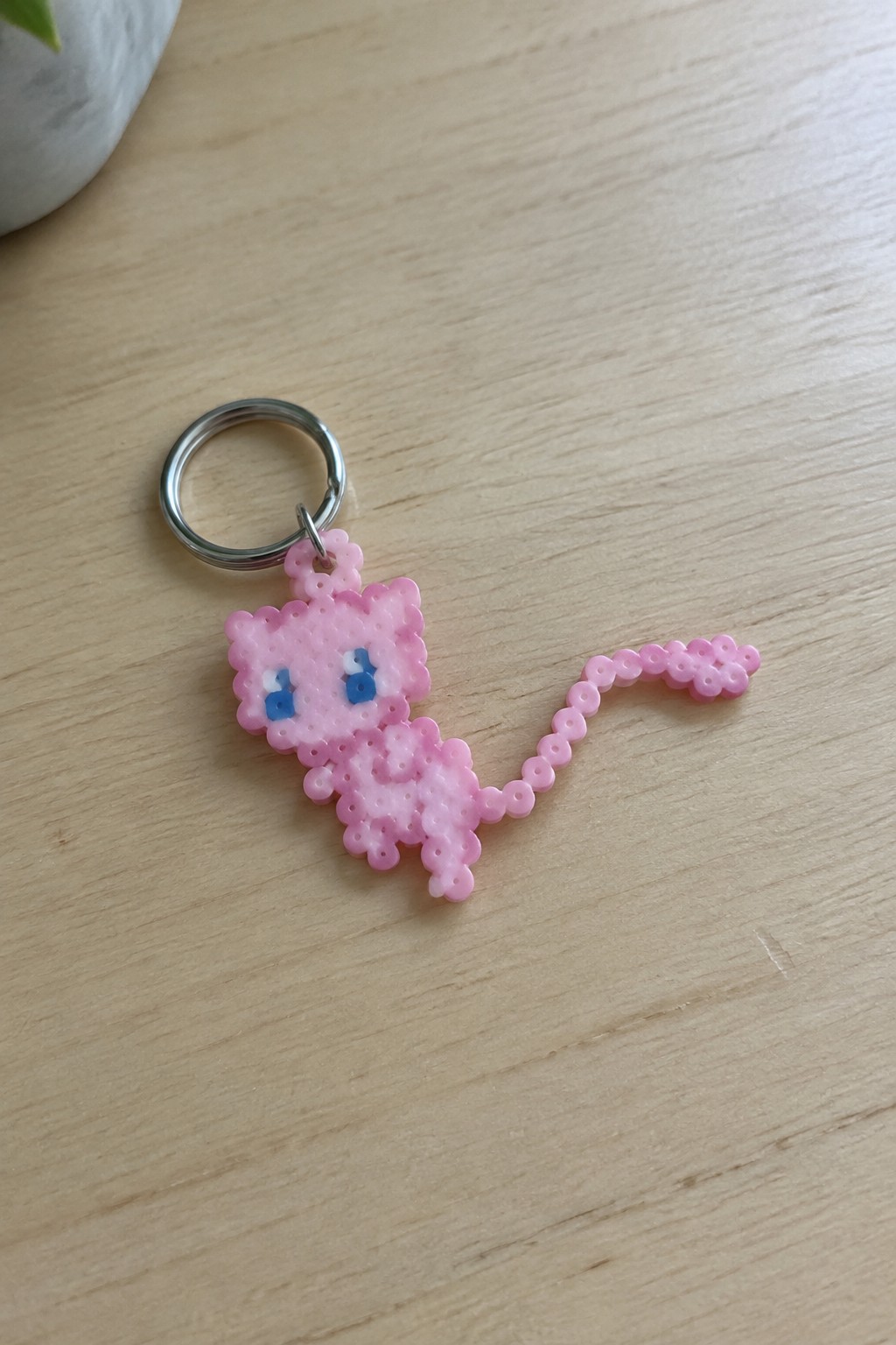 Pink perler bead Mew keychain with blue eyes on wooden table