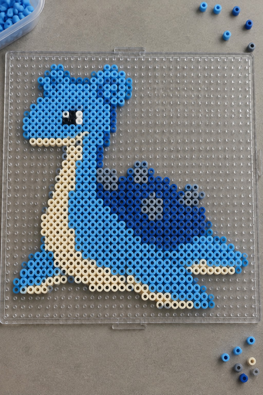 Blue perler bead animal figure on clear pegboard with scattered loose beads