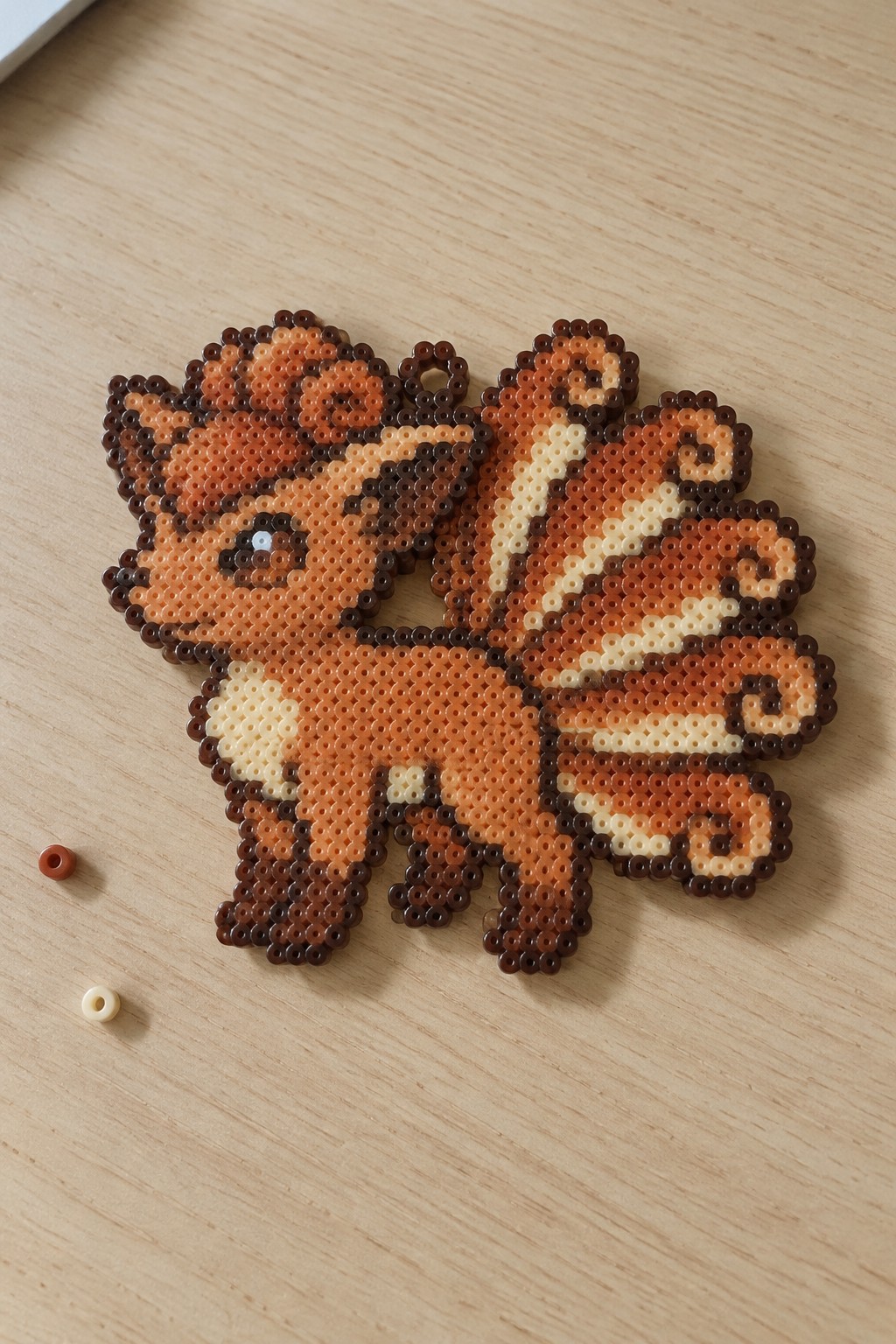 Orange-brown perler bead fox with multiple tails on light wood table