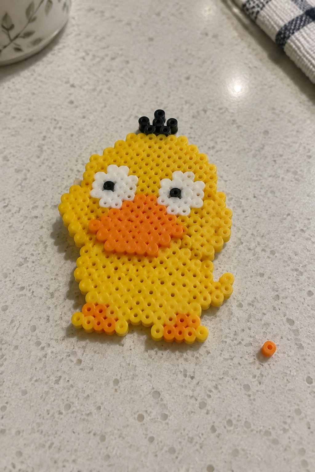 Yellow perler bead chick with orange beak, feet, and black head beads