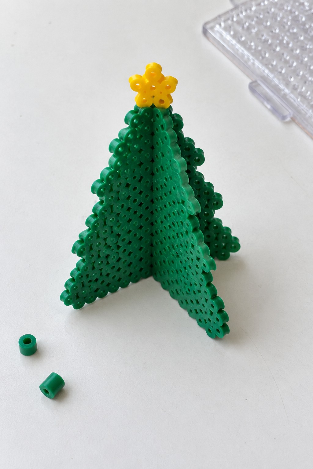 Green Perler bead Christmas tree with yellow star topper and loose beads nearby