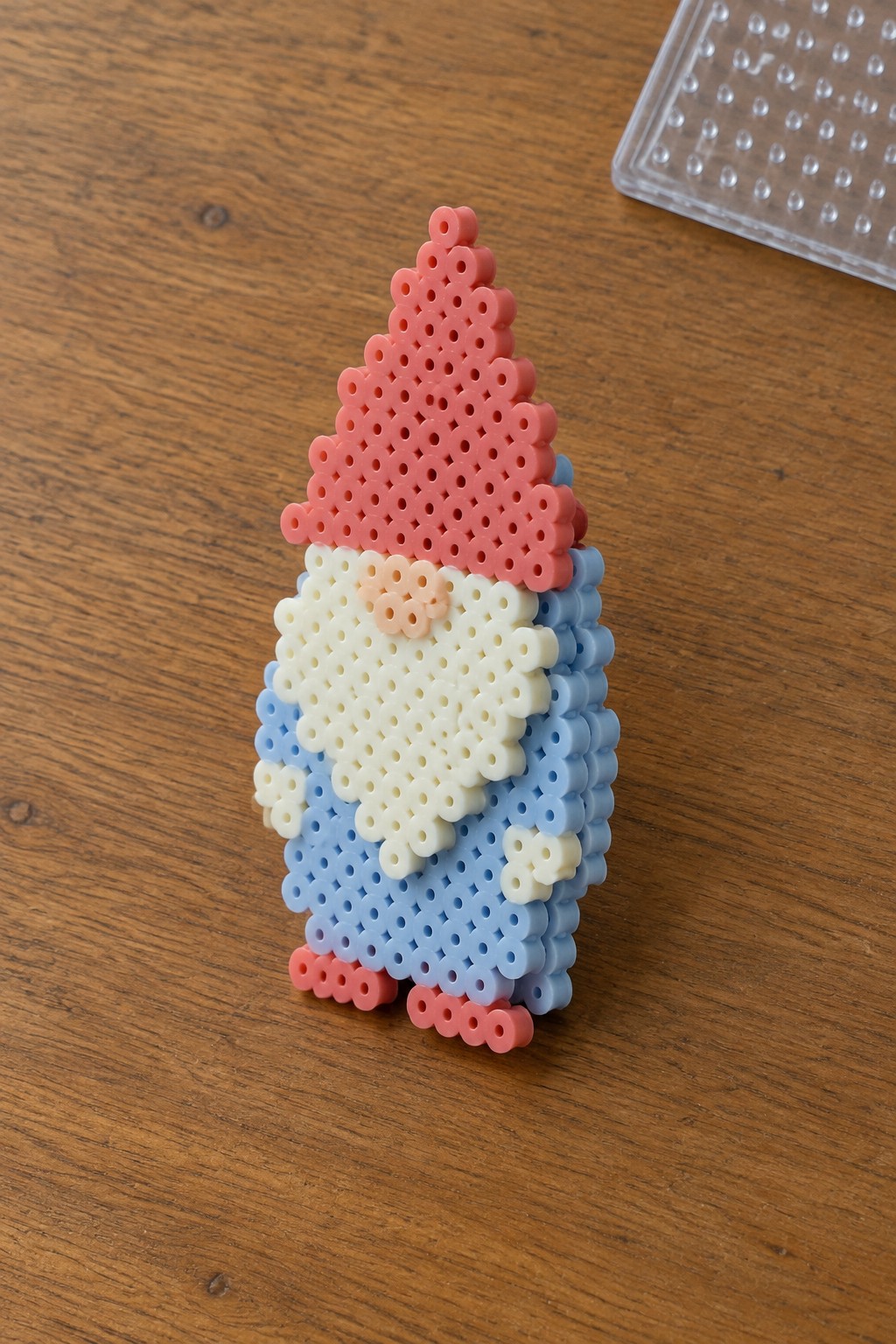 Perler bead gnome with pink hat, white beard, blue outfit on wooden table