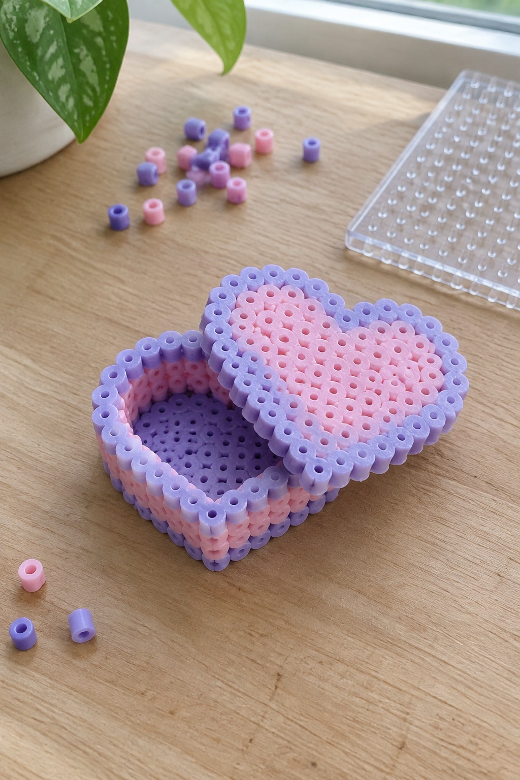 Open heart-shaped pink-purple perler bead box on wood table with scattered beads