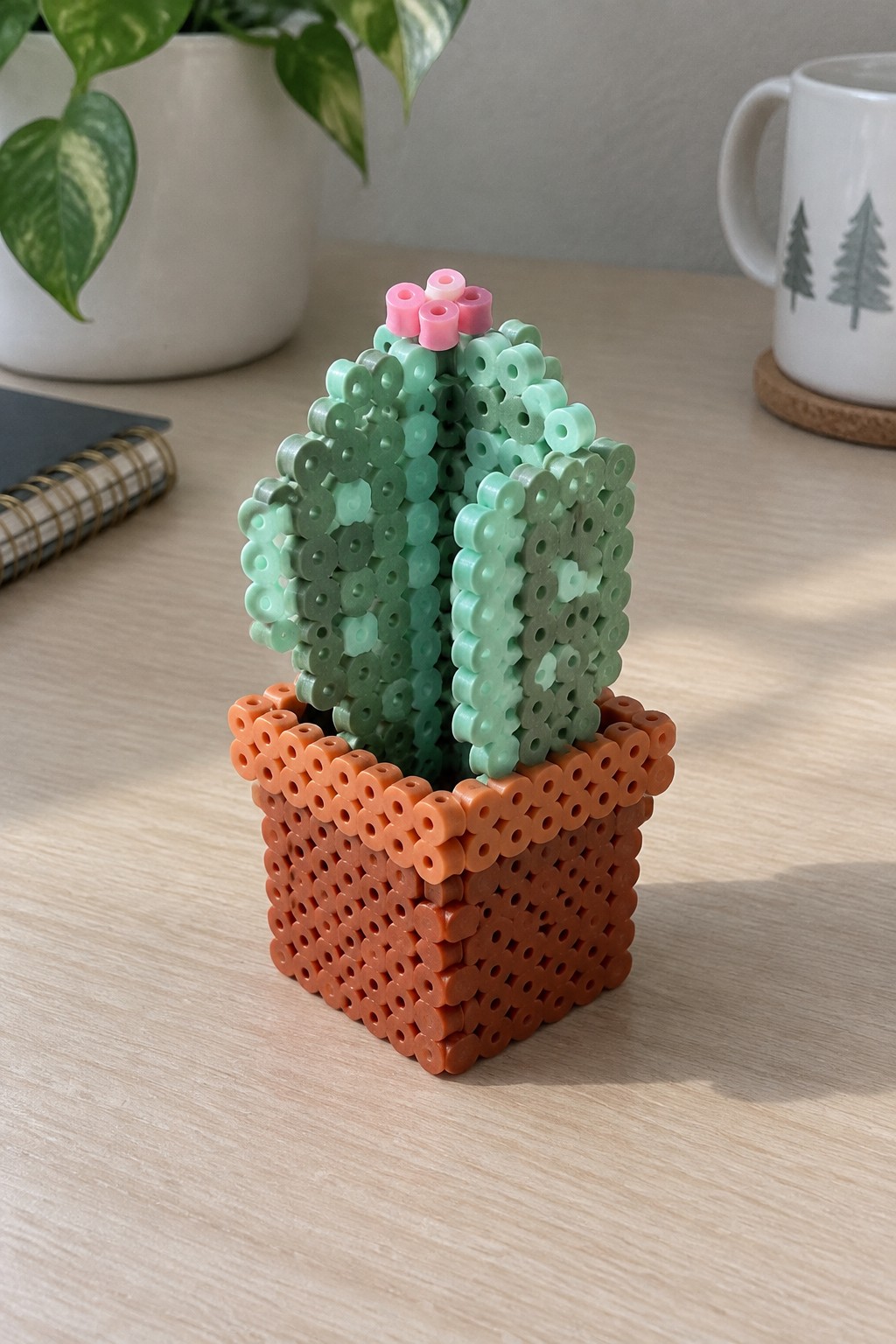Green perler bead cactus with pink flowers in orange pot on wooden desk