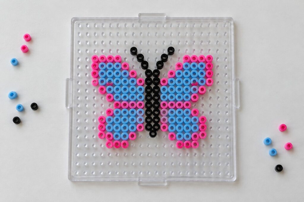 Perler bead butterfly with pink and blue symmetrical wings and black body on a pegboard.