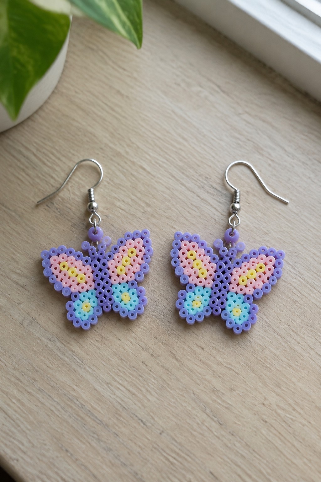 Pastel perler bead butterfly earrings with silver hooks on wooden surface