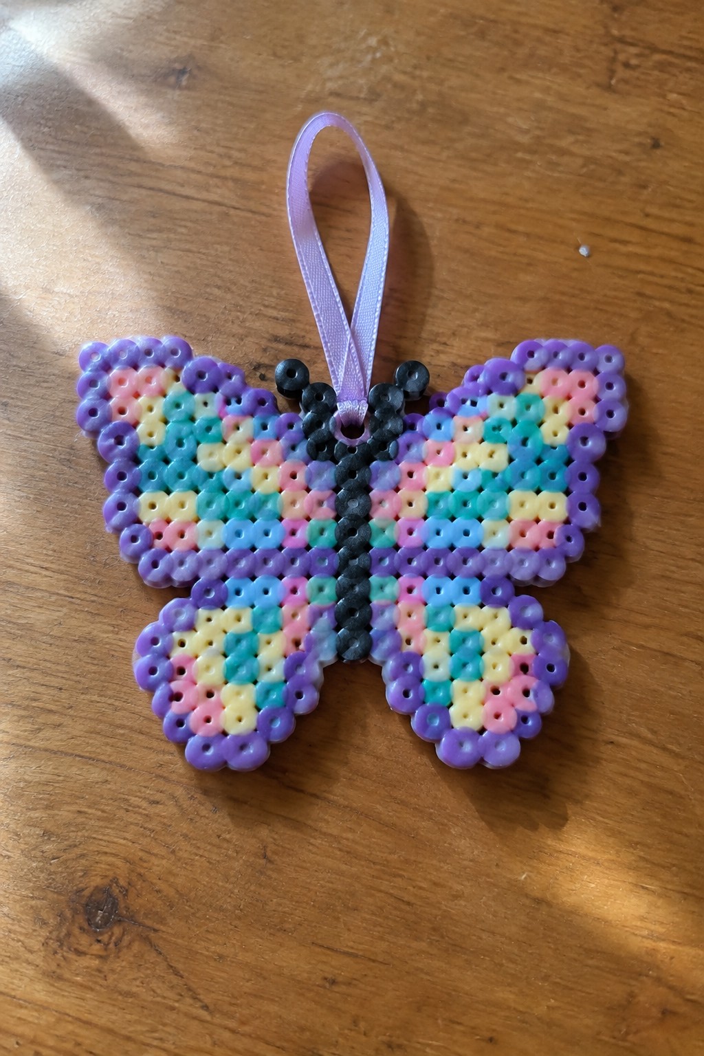 Colorful perler bead butterfly with black body and purple ribbon on wood