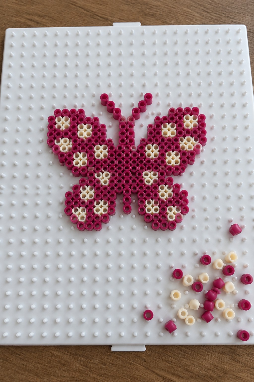 Pink and cream beaded butterfly on white pegboard with scattered loose beads