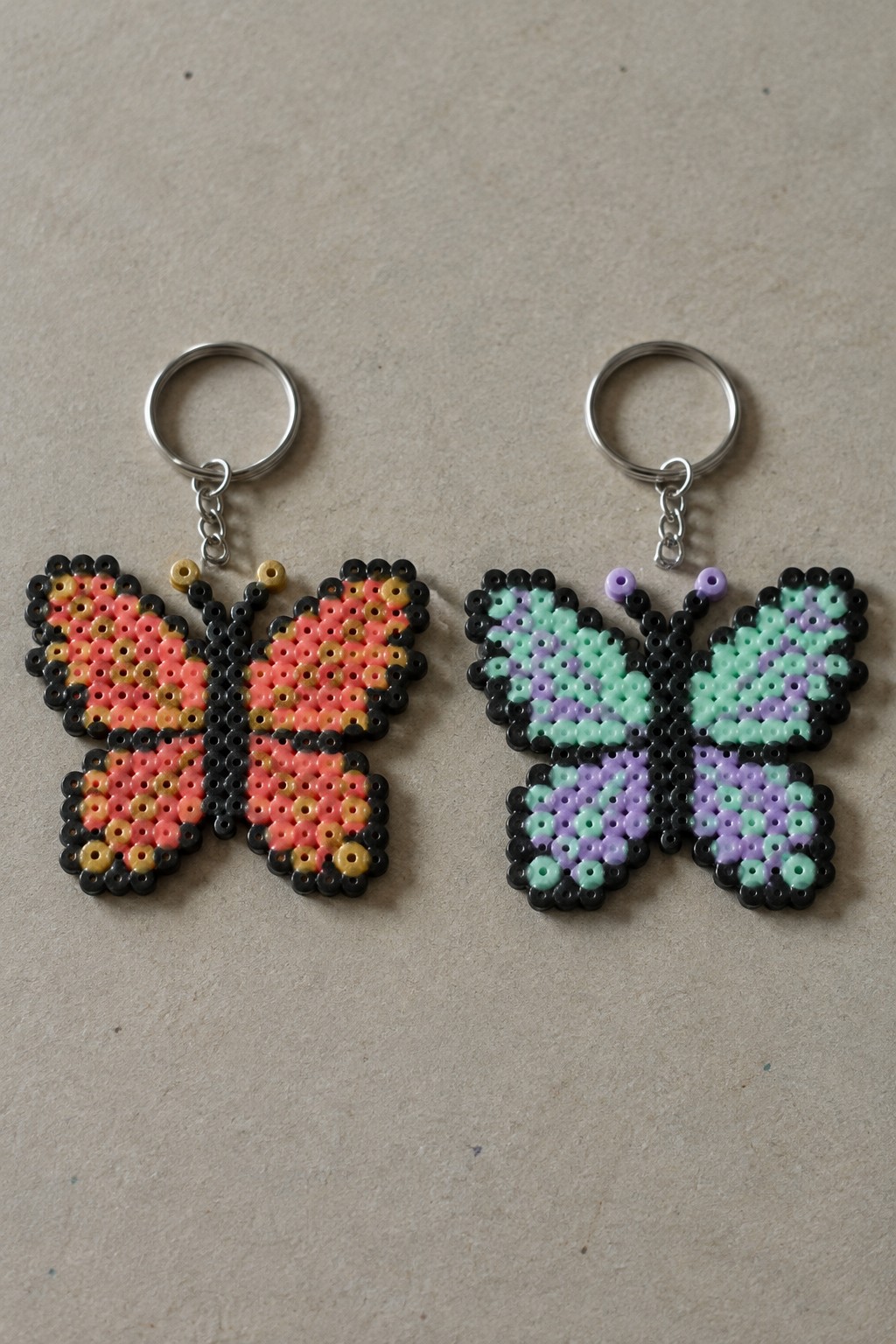 Two perler bead butterfly keychains in orange-pink and mint-purple with silver rings.