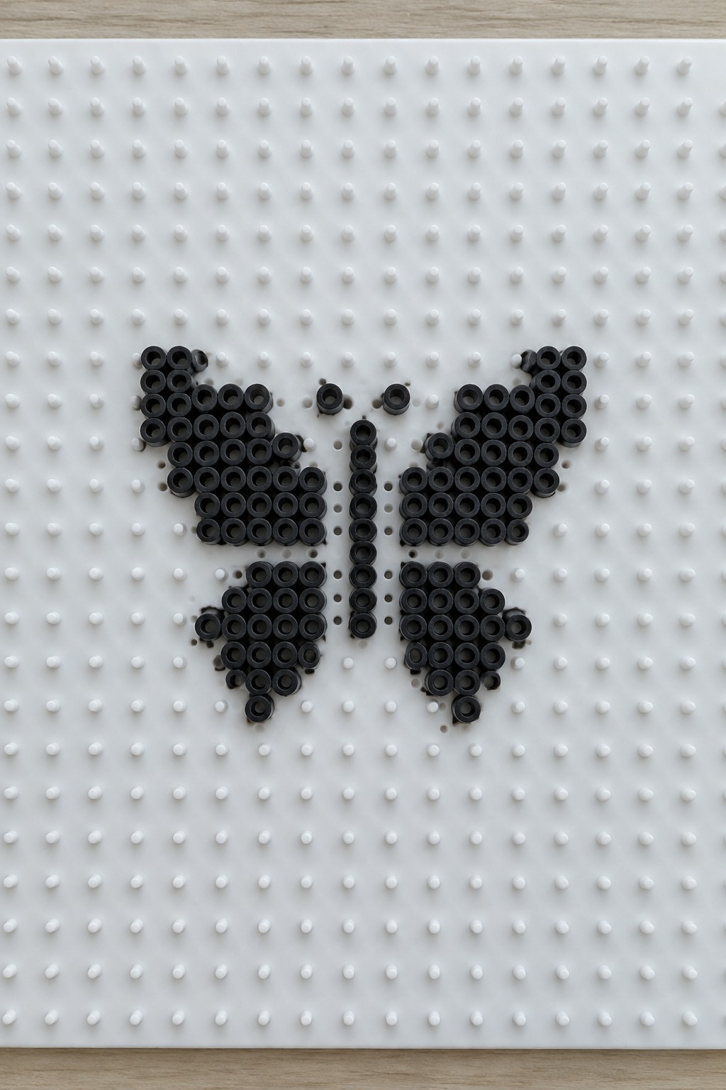 Black Perler bead butterfly design on a white pegboard.