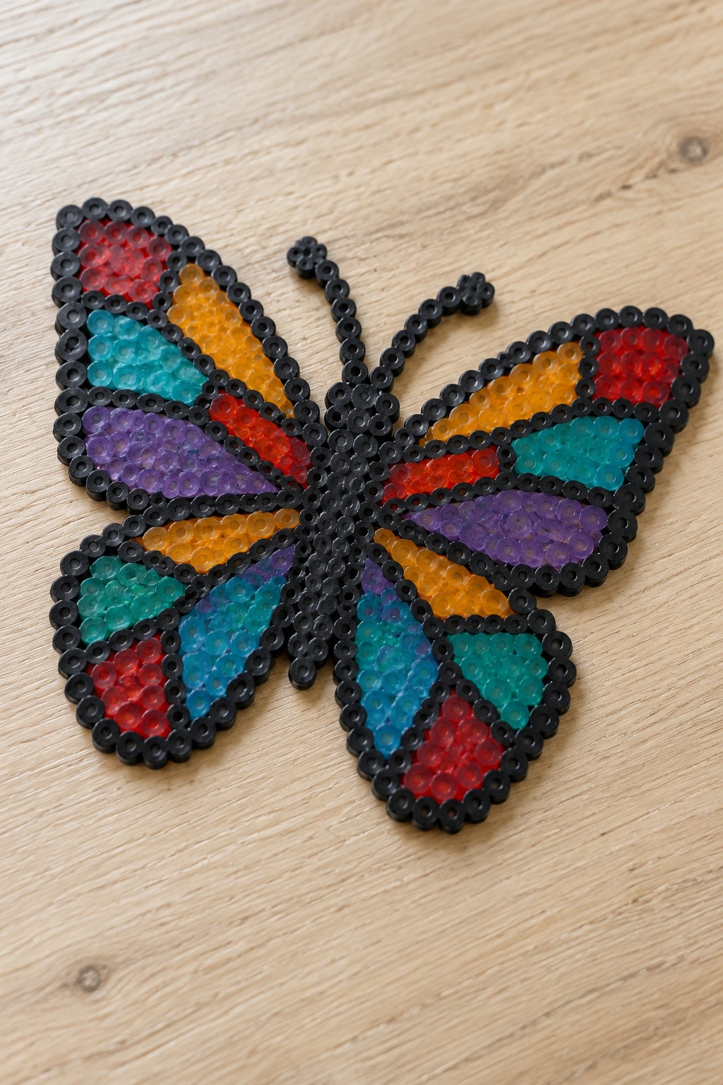 Colorful perler bead butterfly with rainbow wings and black outline on wood