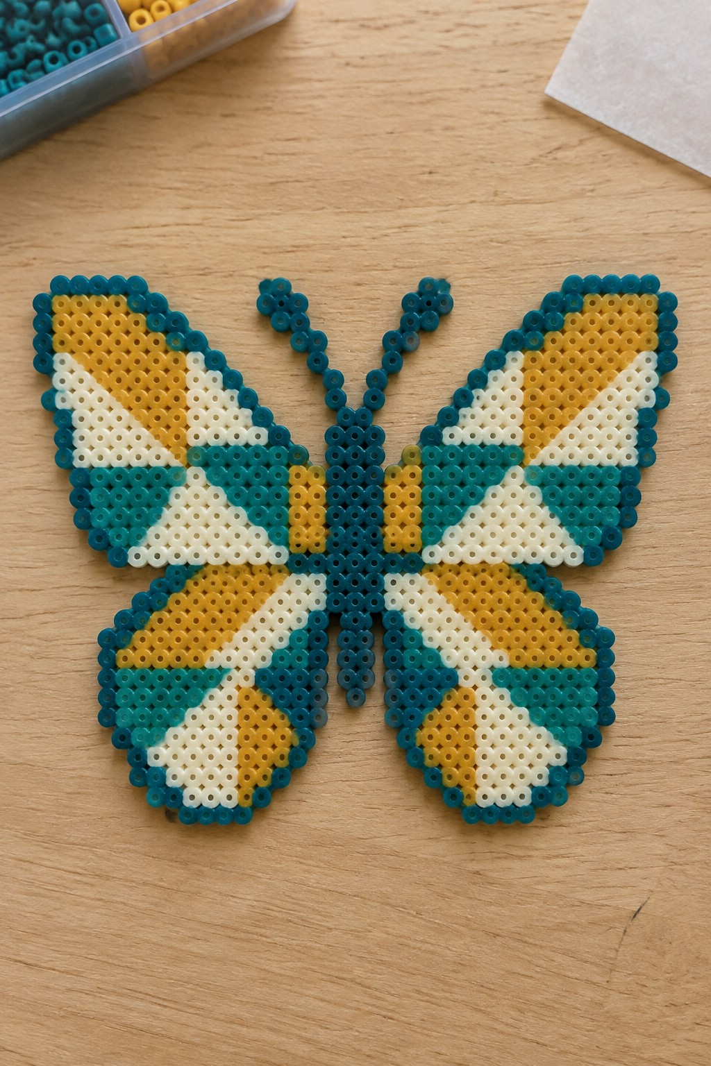 Teal, yellow, and white perler bead butterfly with antennae on wooden table