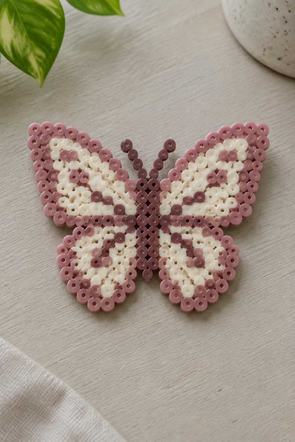 Pink and white perler bead butterfly with antennae on light wood surface
