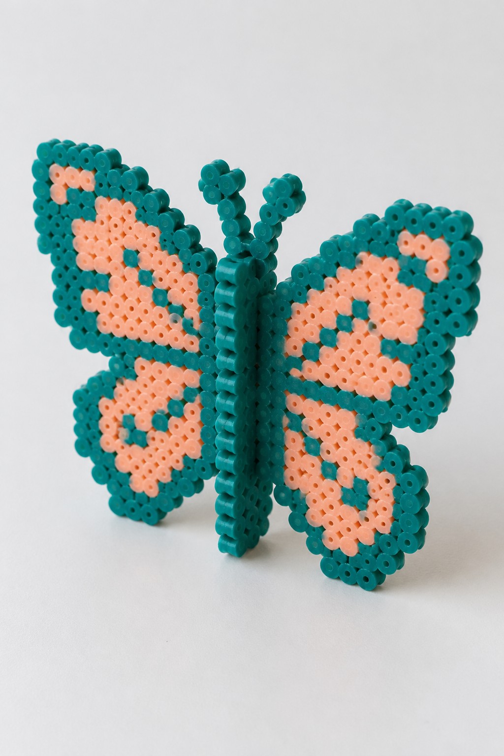 Teal and peach perler bead butterfly with patterned wings and antennae