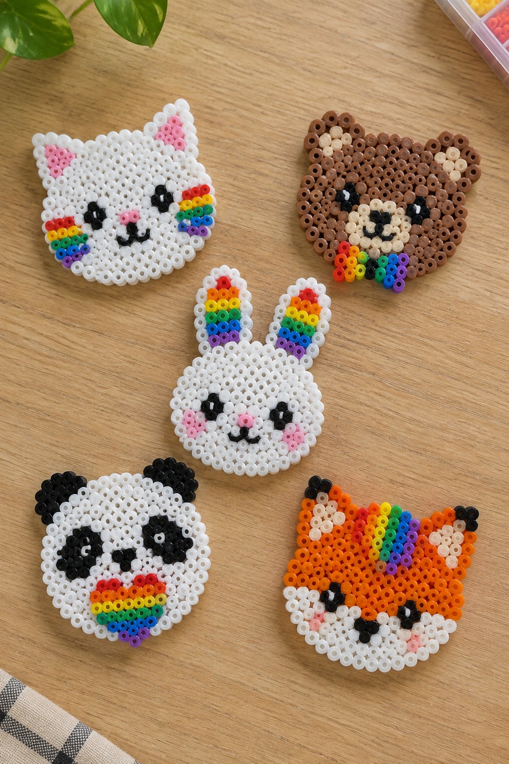 Five rainbow-accented perler bead animal faces on wooden table.