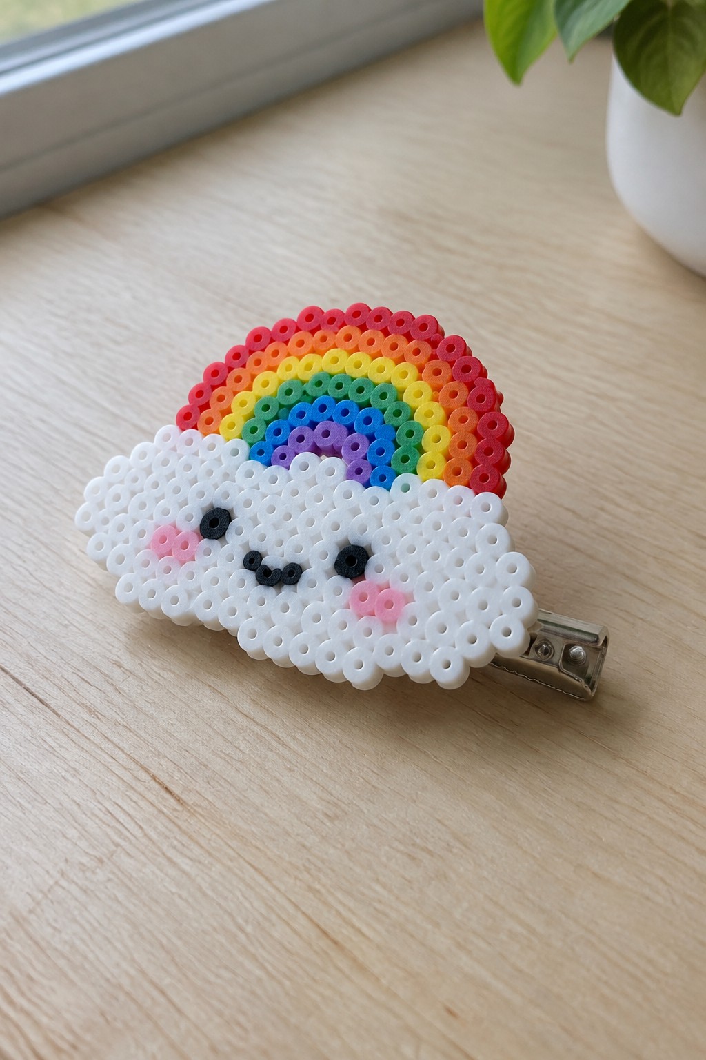Fused Perler bead hair clip with a white cloud face and rainbow arch.