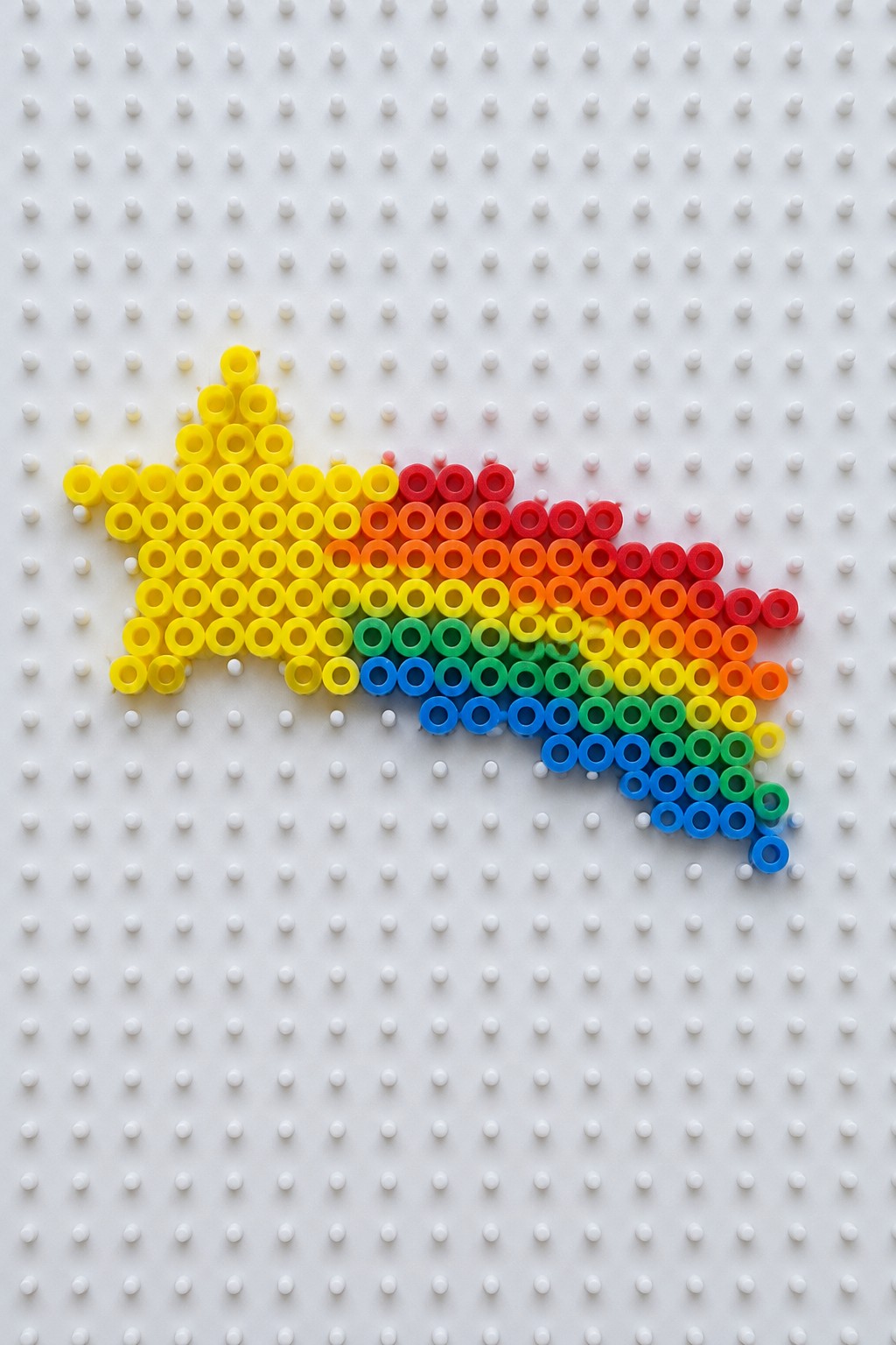 Rainbow perler beads forming a comet shape on white pegboard.