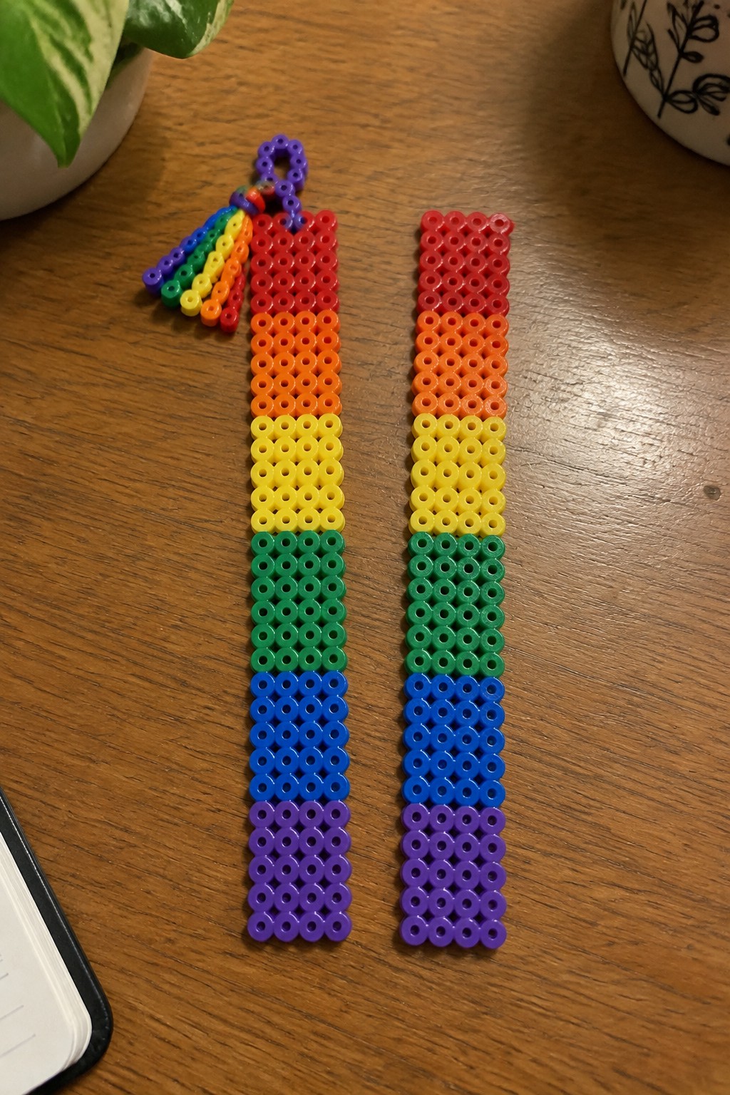Two rainbow Perler bead crafts on wooden table, one with tassel.