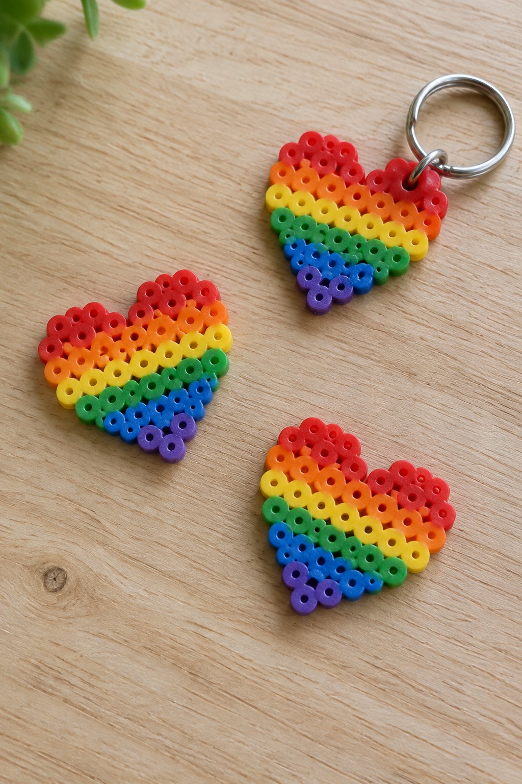 Three rainbow perler bead hearts on wood, one with metal keyring attached