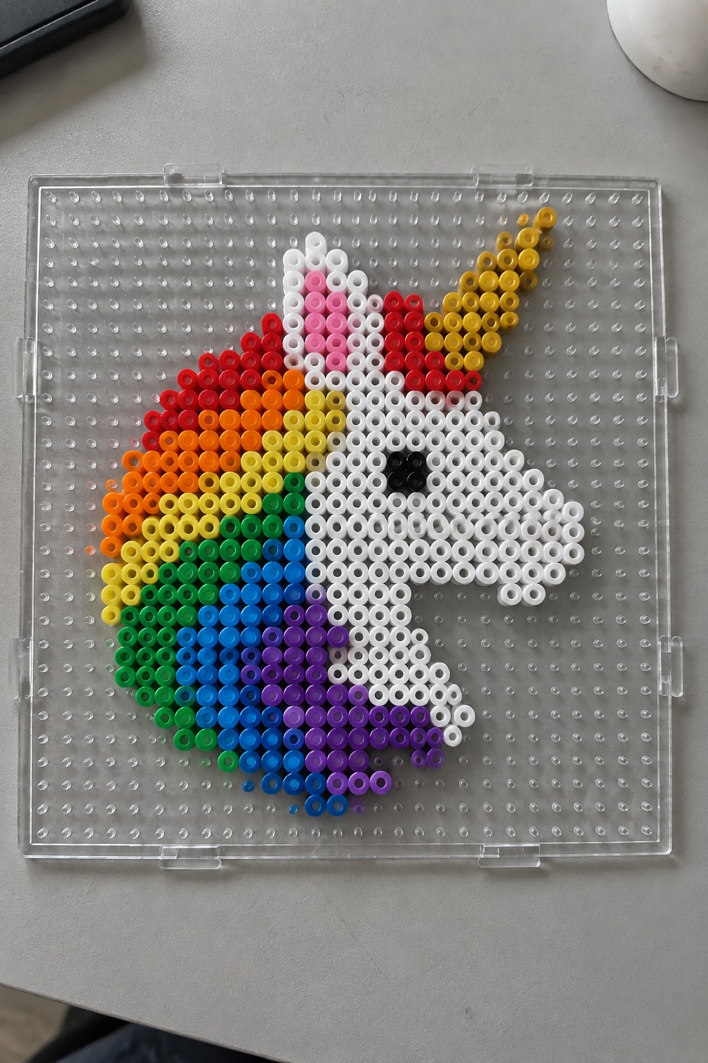 Unicorn Perler bead design in rainbow colors on a clear pegboard.