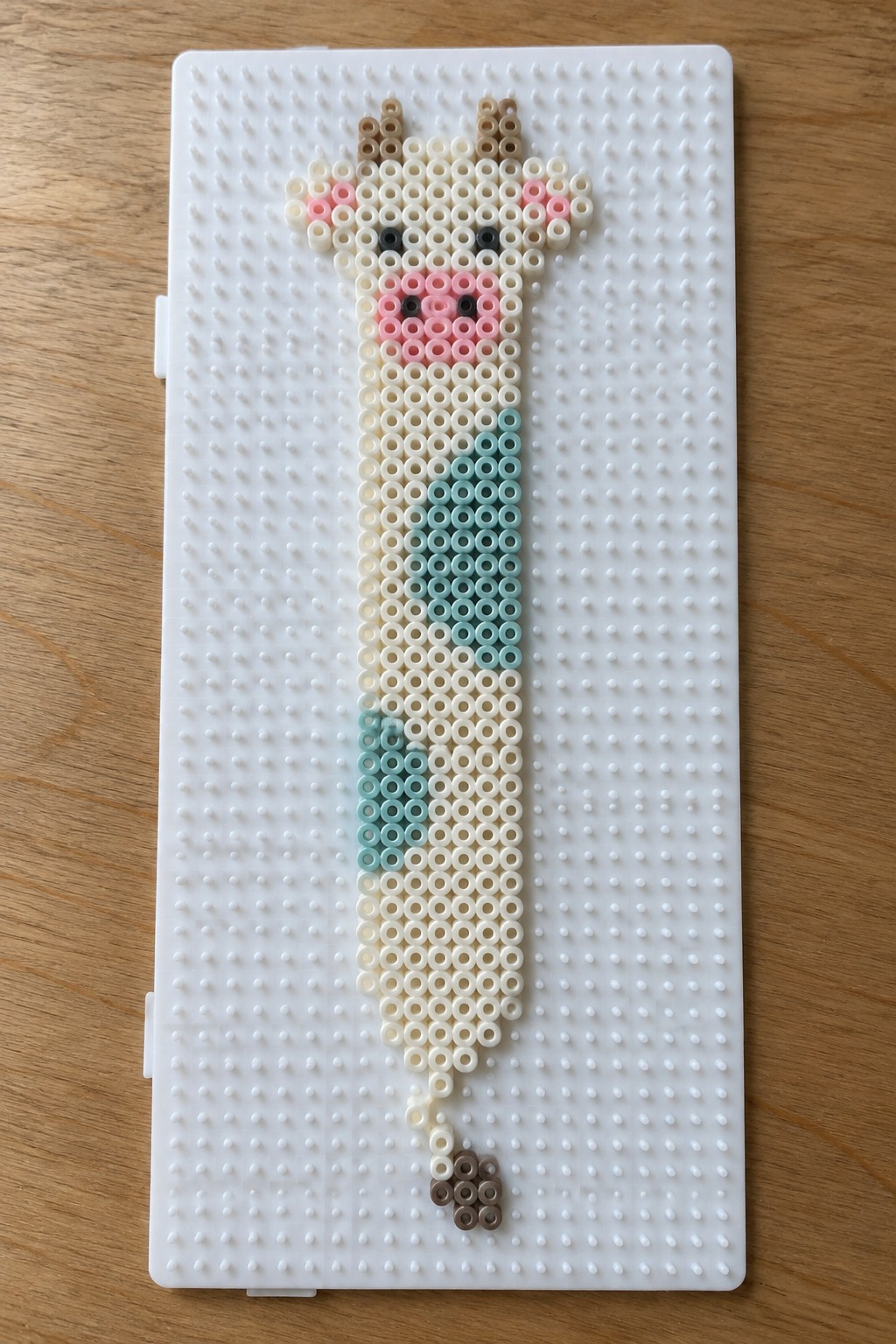 Perler bead giraffe with pink cheeks and blue neck pattern on white pegboard