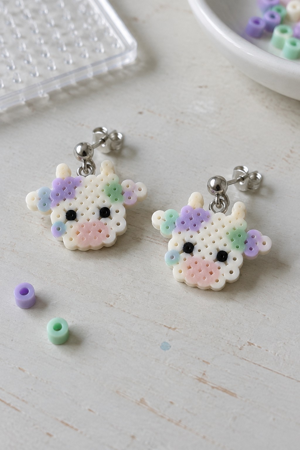 Two pastel perler bead cow earrings with silver studs on wooden surface