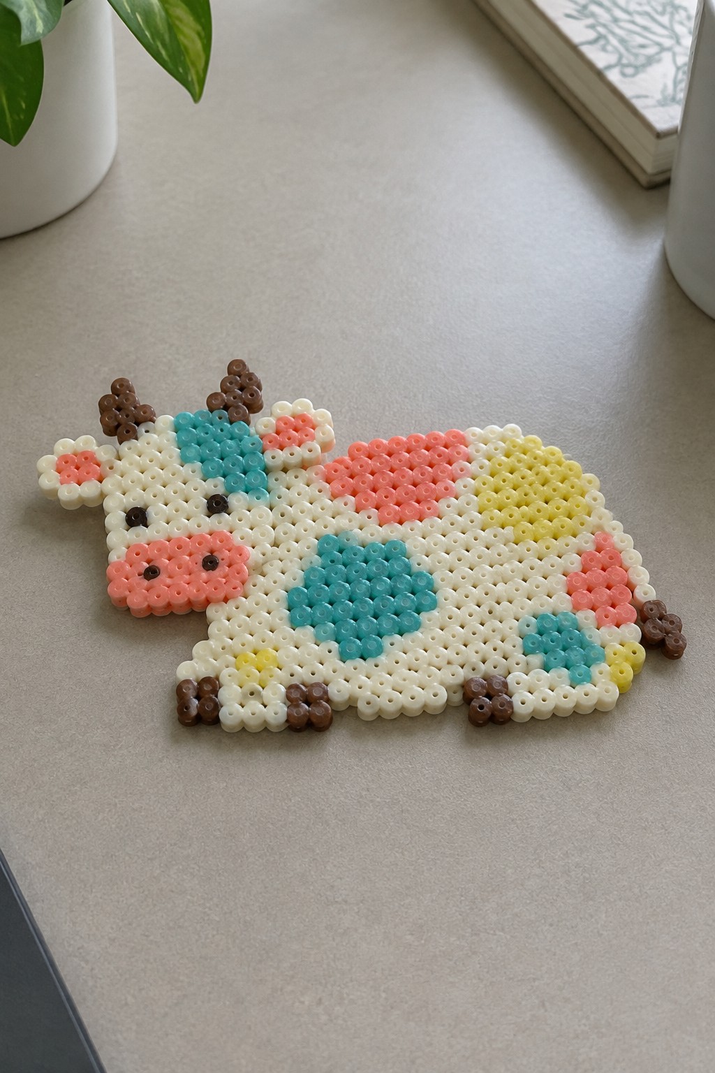 Colorful perler bead cow with pink turquoise spots on light tabletop