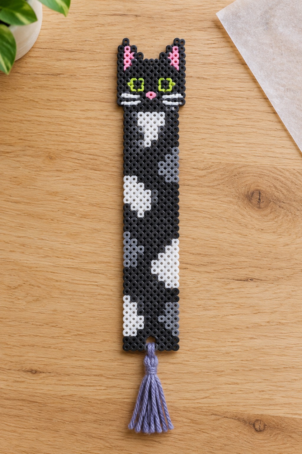 Black perler bead cat bookmark with white patches, pink ears and purple tassel.