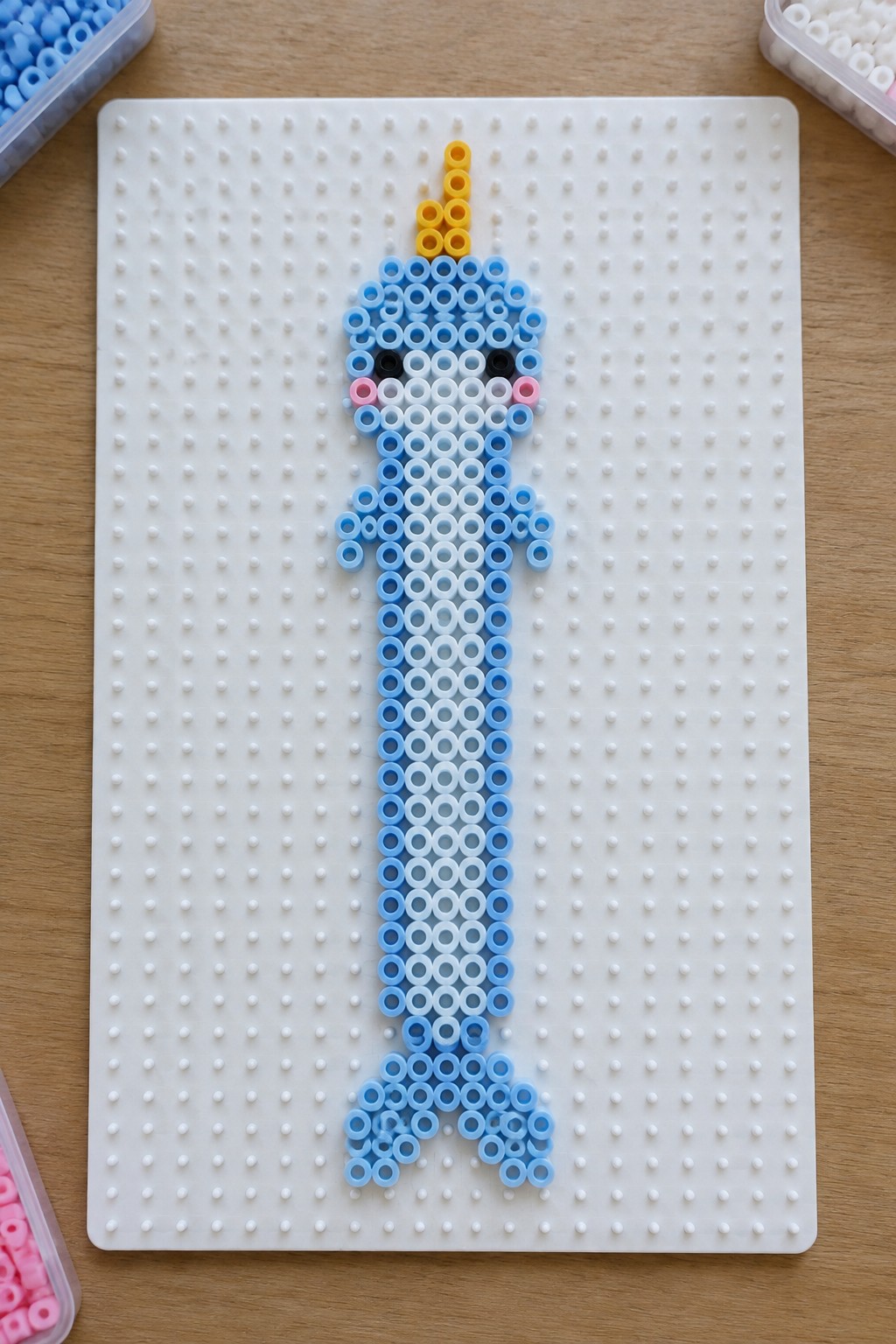 Blue gradient perler bead narwhal with yellow horn on white pegboard