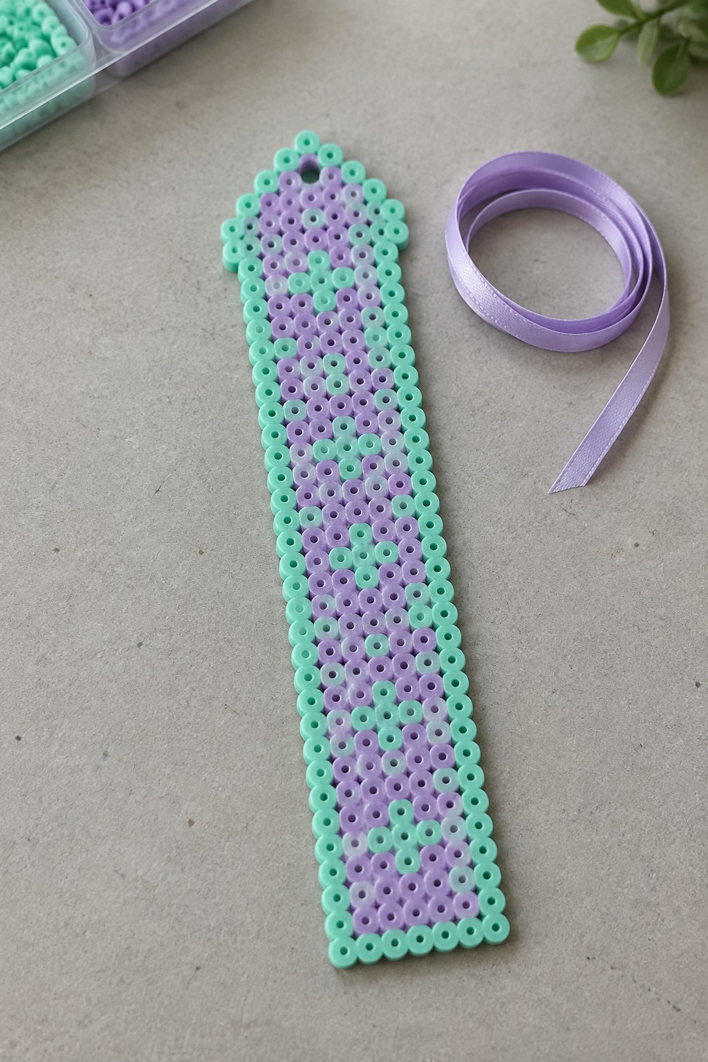 Turquoise and purple perler bead bookmark beside a lavender satin ribbon