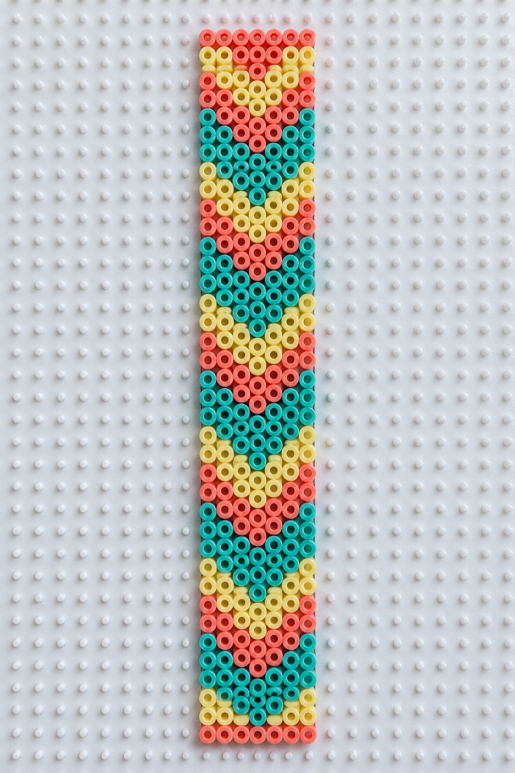 Vertical strip of coral, yellow, and teal beads forming pattern on pegboard.