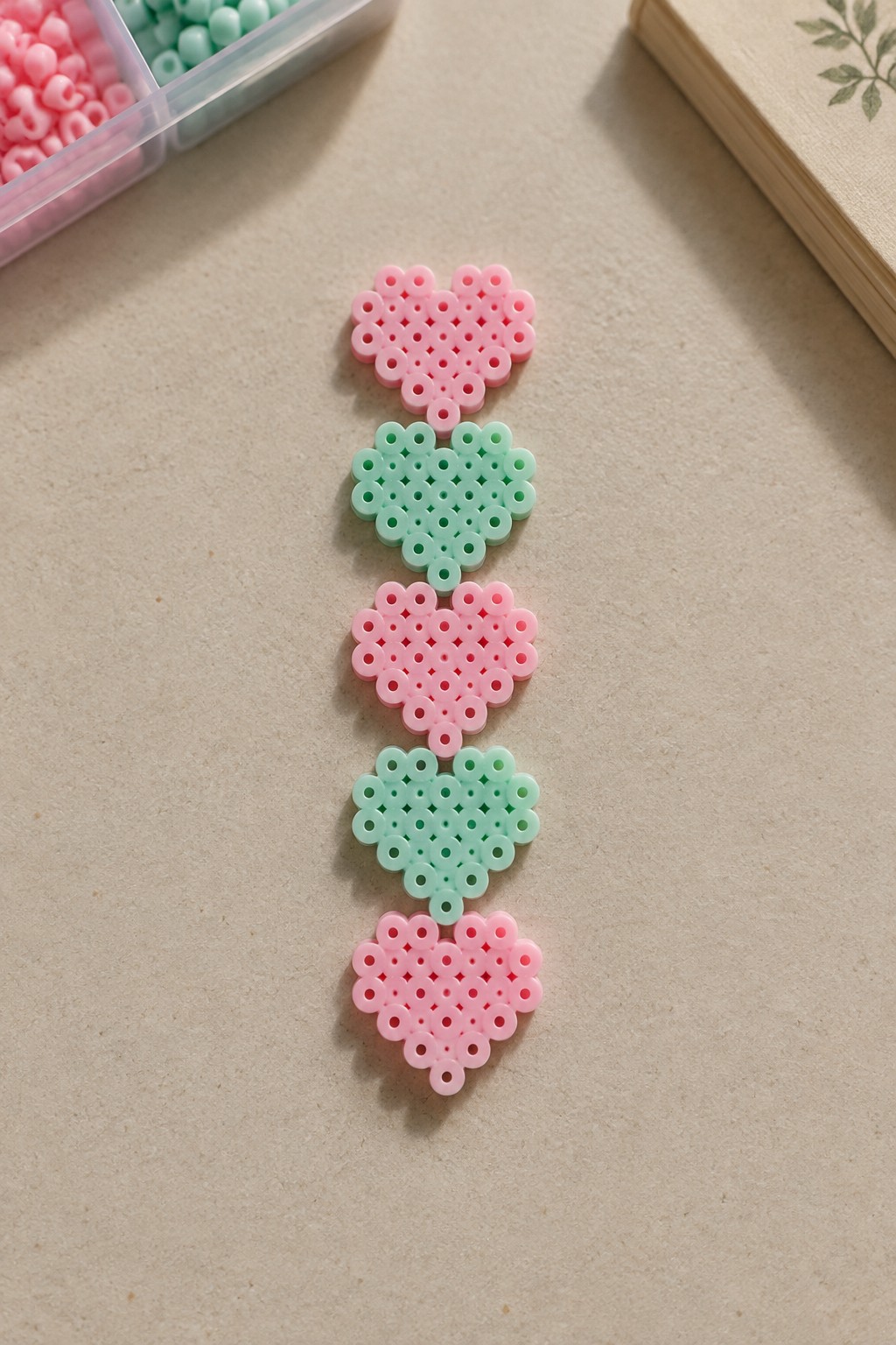Vertical row of pink and mint green heart perler bead crafts with supplies.