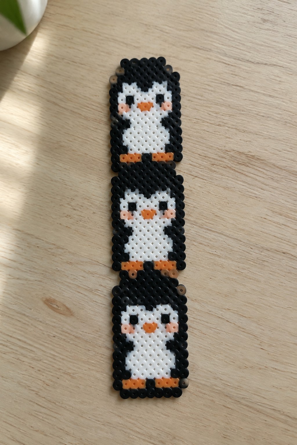Three stacked perler bead penguins in black, white, and orange on wood.