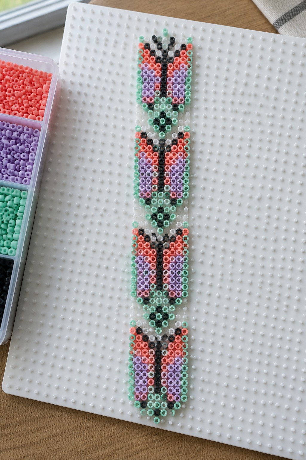 Three colorful tulip patterns made from perler beads on a white pegboard with bead tray.