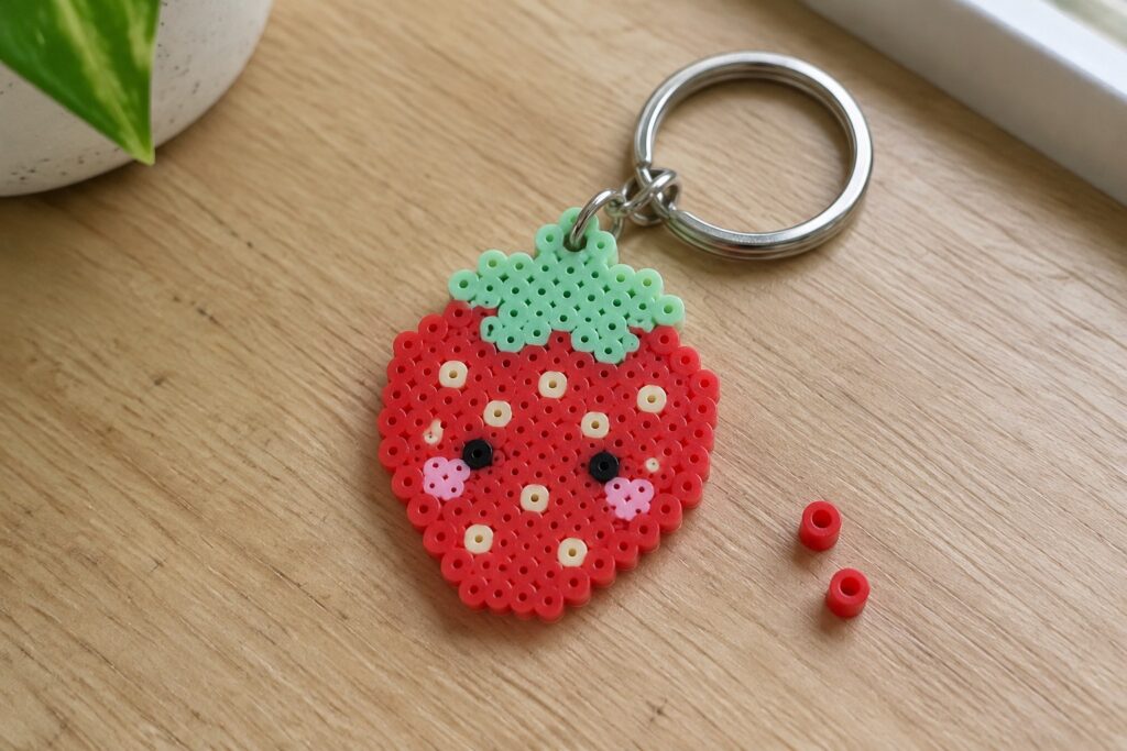 19 Cute Perler Bead Ideas Featuring Kawaii Food Characters Perler bead strawberry keychain with pink border, green leaves, and cute face