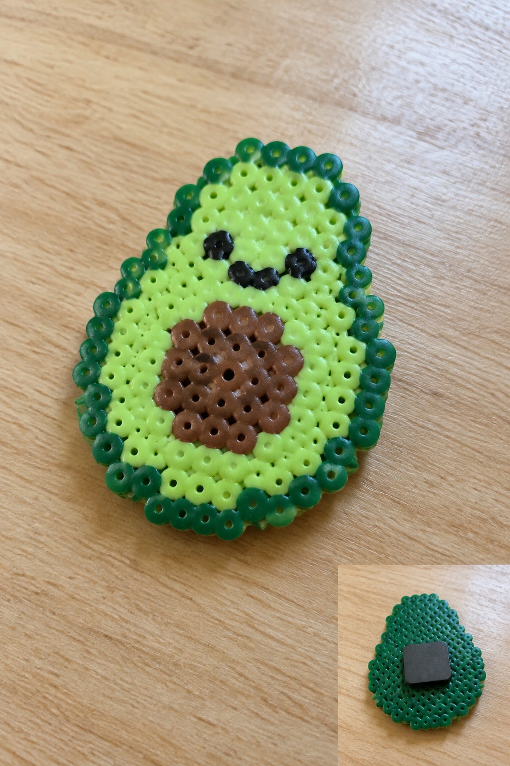 Perler bead avocado magnet with smiling face on wooden surface, back view inset