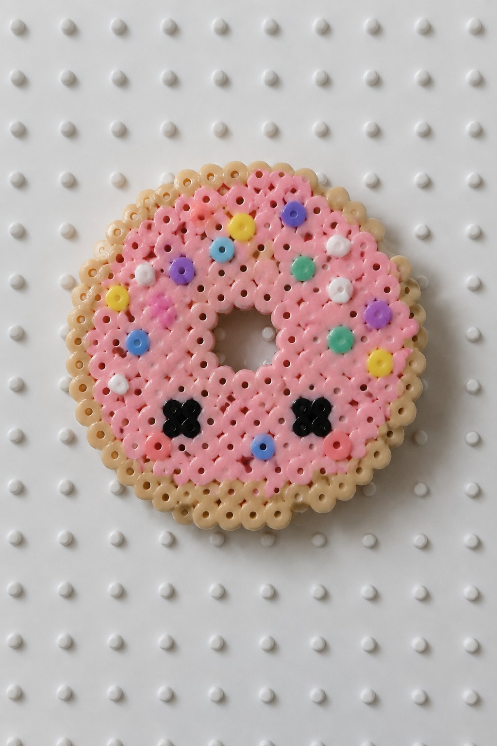 Pink perler bead donut with colorful sprinkles and cute face on pegboard