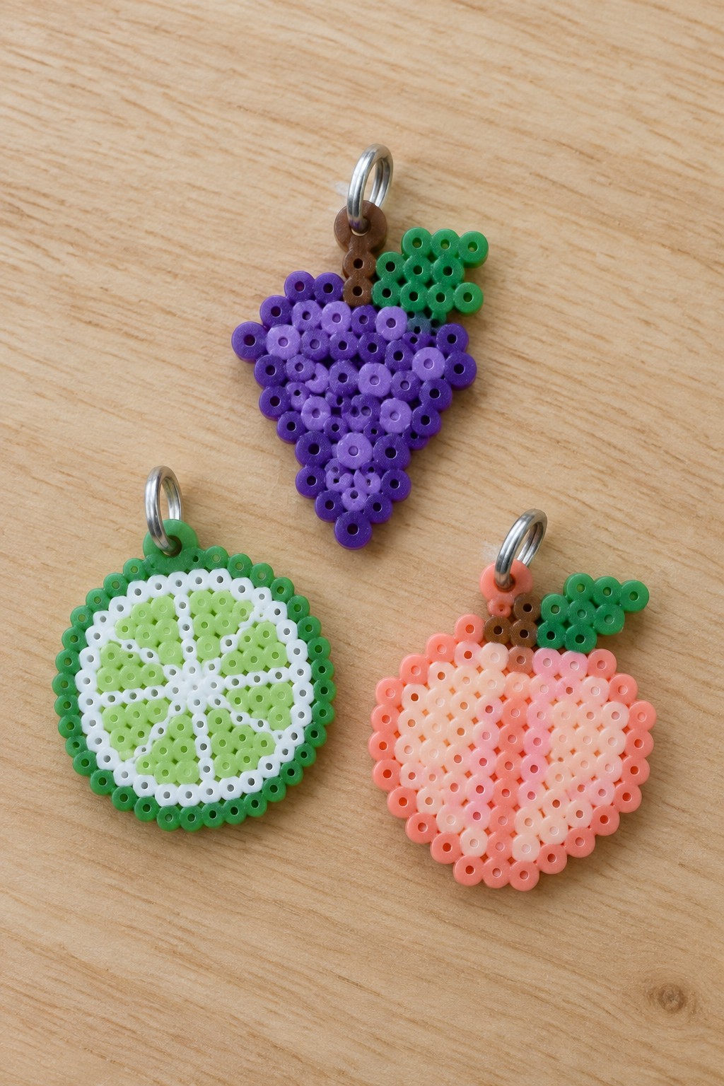 Three perler bead fruit charms: lime slice, grapes, and peach on wood
