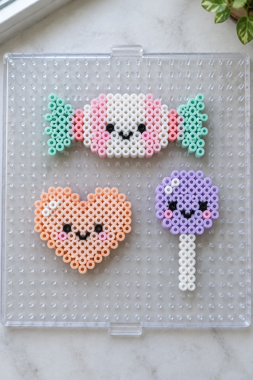 Perler bead crafts of cat face, peach heart, and purple lollipop on pegboard