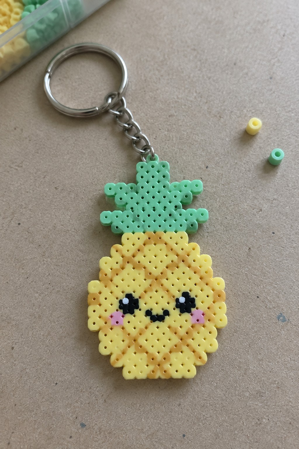 Yellow perler bead pineapple keychain with smiling face and green leaves on metal ring