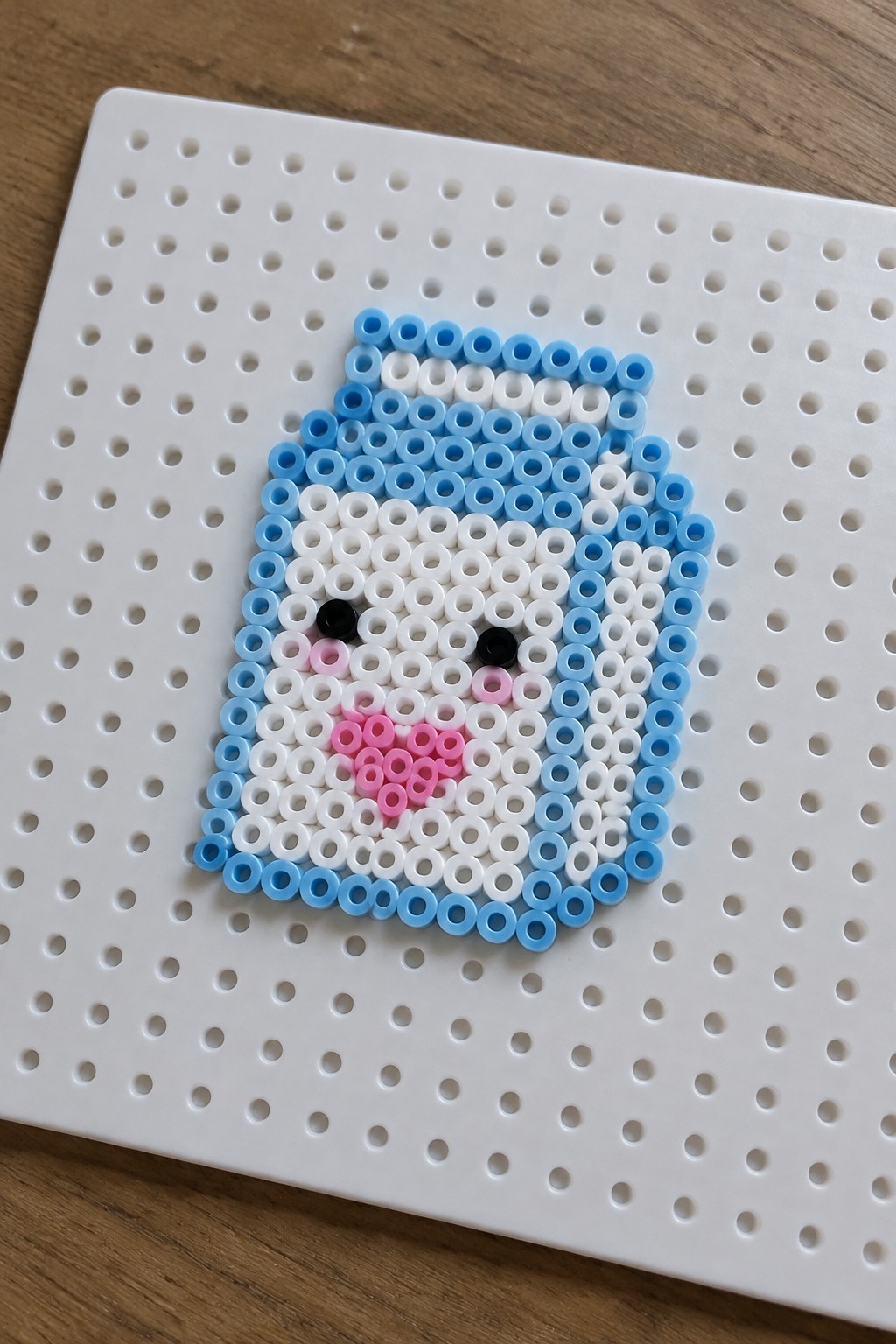 Perler bead craft of blue-bordered white face with pink accents on pegboard